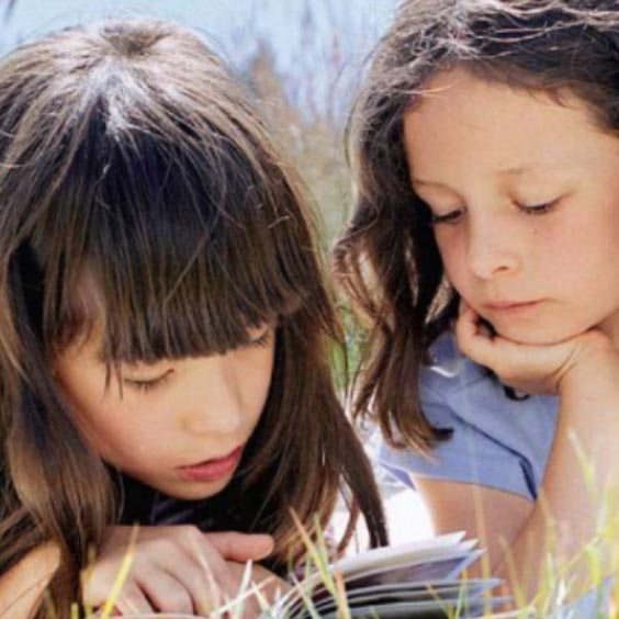 Two girls reading a book outside