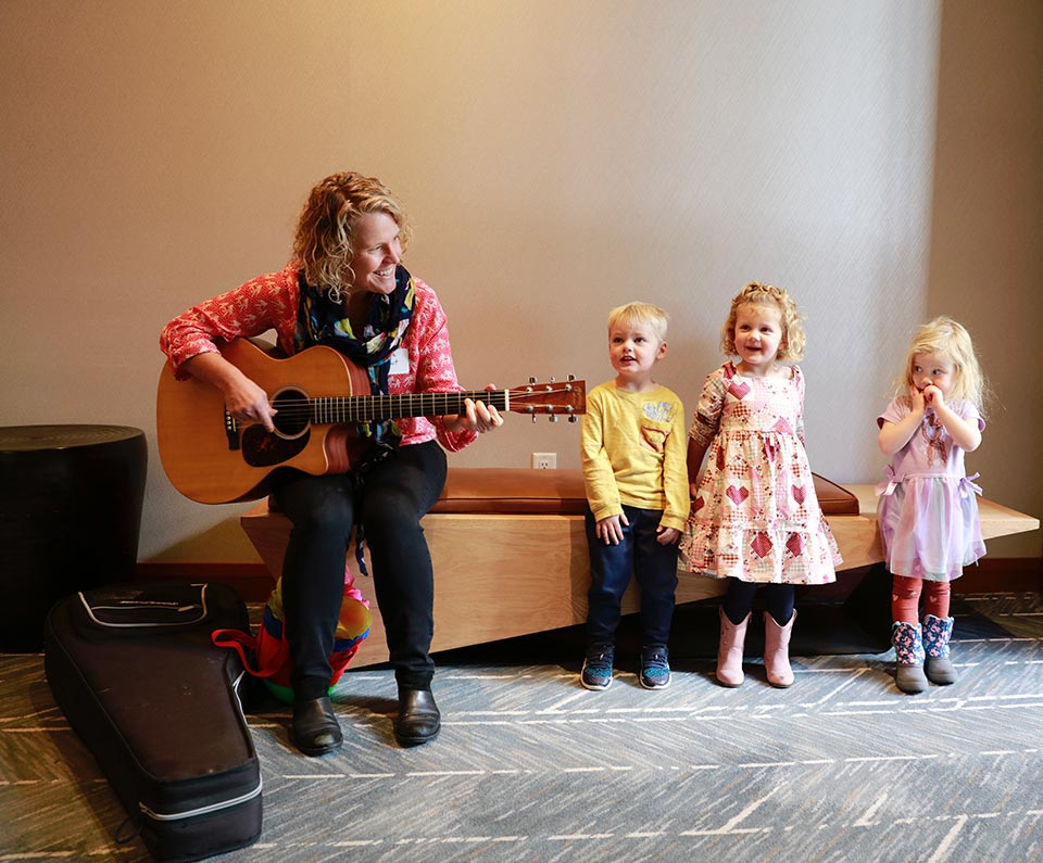 Brooke playing guitar with three children at the KidZone's Think Big fundraiser
